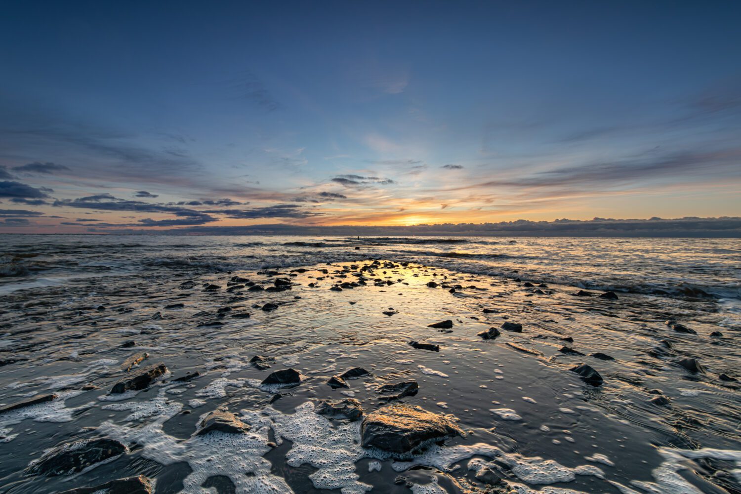 De ondergaande zon geeft de lucht, het terugtrekkende zeewater en de stenen van de pier een warme gloed