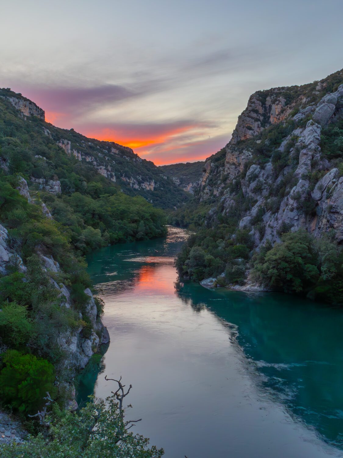 Het water van de Gorges du Verdon stroomt langzaam tussen de bergen door terwijl de ondergaande zon de lucht rood doet kleuren