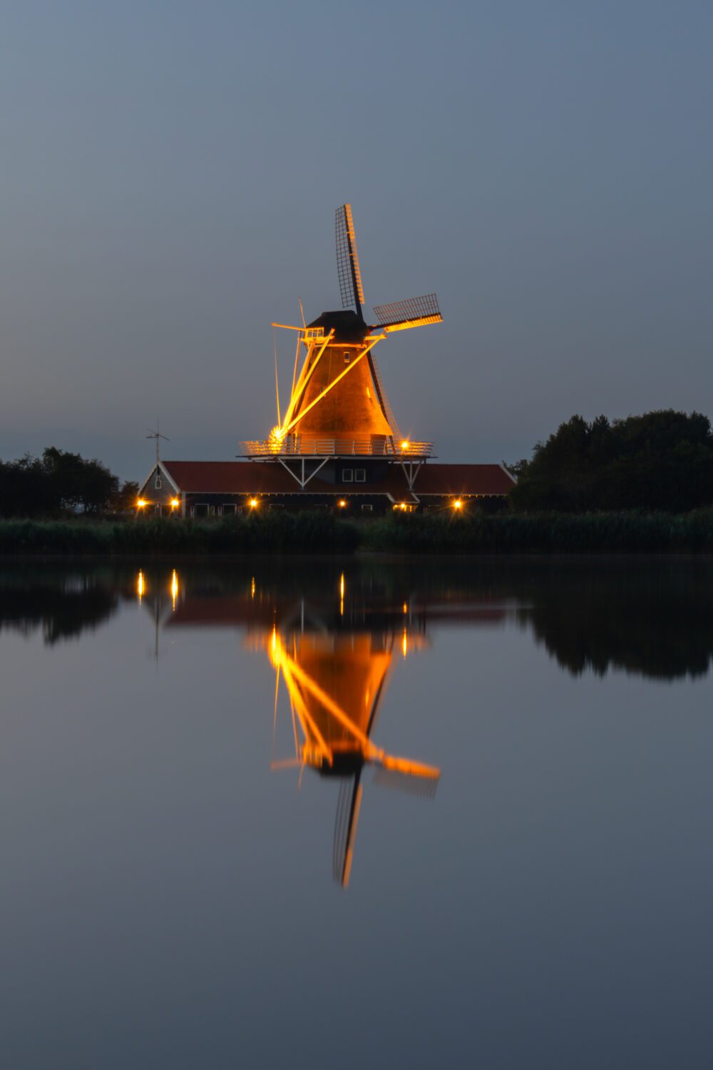 De verlicht molen aan het Oude Veer in Anna Paulowna tijden het blauwe uur voor zonsopkomst weerkaatst in het rustige water