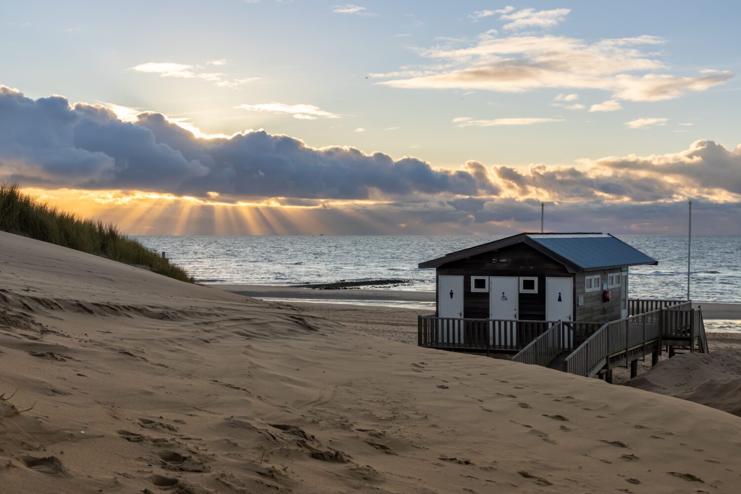 Een blik vanaf de duinen op het redding huis op het strand en zonneharpen door de wolken boven de Noordzee