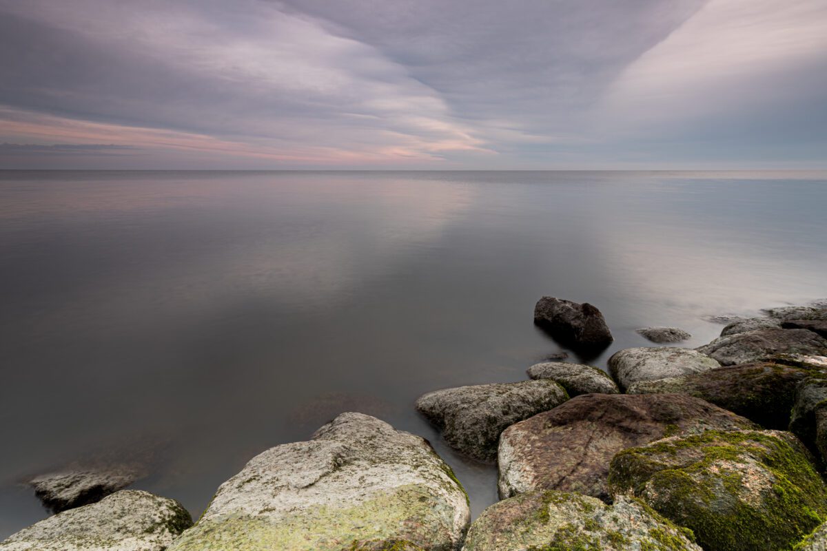 Stenen in het rustige water van het Markermeer bij Edam, waar de kleurrijke wolken een X vormen