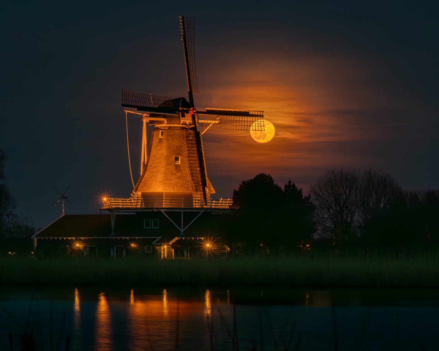 De sluierbewolking verzacht het felle volle maanlicht dat door de wieken van de verlichte molen schijnt