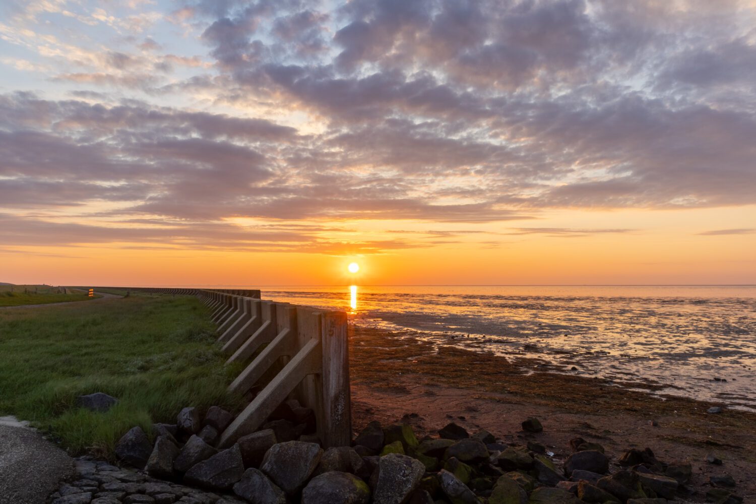 Gekleurde wolken boven de Waddenzee bij de zeewering en stenen op Wieringen tijdens zonsondergang